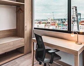 In-room workspace featuring a desk, ergonomic chair, coffee station, mini-fridge, and large window overlooking the port at Holiday Inn Express Cartagena Manga.