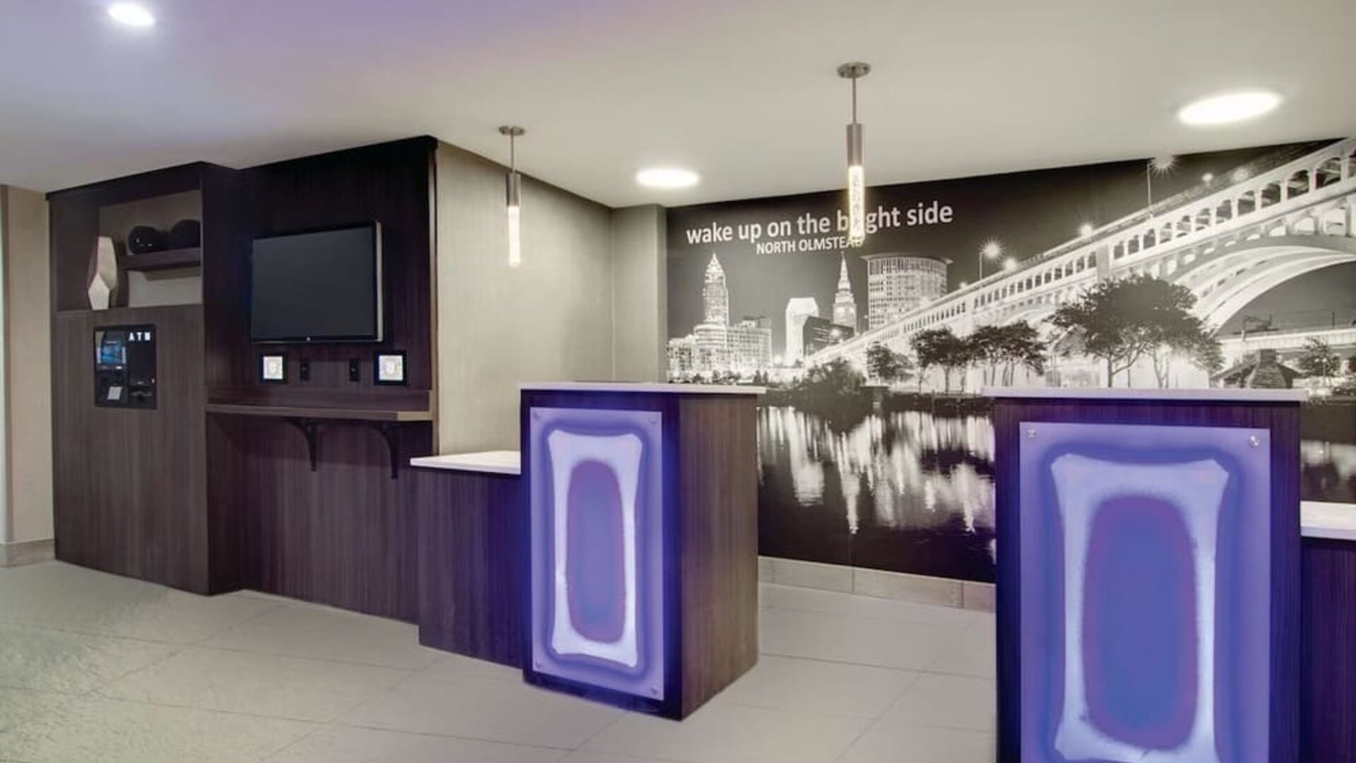 Modern reception area featuring illuminated front desks and a Cleveland cityscape mural at La Quinta Inn & Suites By Wyndham Cleveland Airport West.
