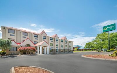 Exterior of Quality Inn with beige four-story building, red roof accents, landscaped entrance, parking area, and hotel sign.
