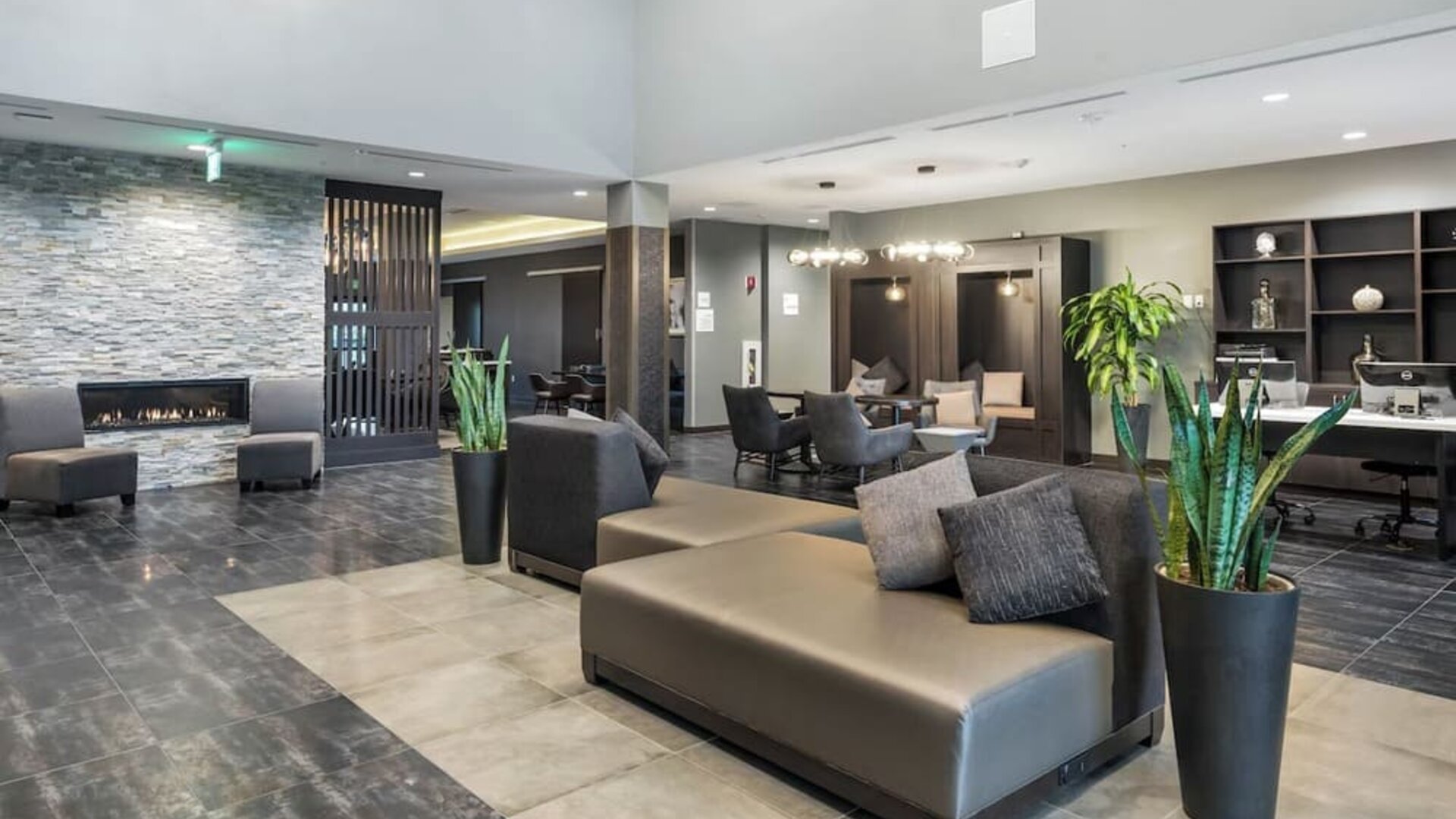 Stylish lobby seating area featuring contemporary sofas, a fireplace, plants, and additional lounge seating at Holiday Inn & Suites Silicon Valley - Milpitas.