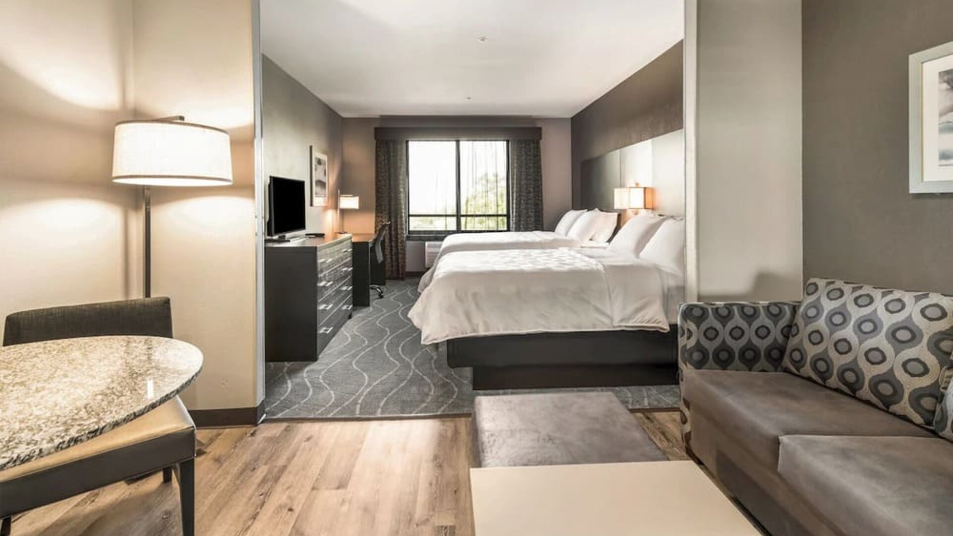 Spacious suite featuring two beds, a separate lounge area with sofa seating, dining space, and contemporary furnishings at Holiday Inn & Suites Silicon Valley - Milpitas.