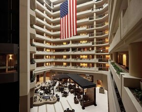 Impressive multi-storey atrium featuring open balconies, lounge seating, dining areas, and a large American flag at Embassy Suites by Hilton Crystal City National Airport.