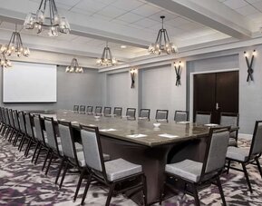 Spacious boardroom featuring a large conference table, ample seating, presentation screen, and contemporary lighting at Embassy Suites by Hilton Crystal City National Airport.