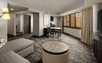 Spacious suite lounge area featuring sofa seating, a work and dining table, television, and large windows at Embassy Suites by Hilton Crystal City National Airport.