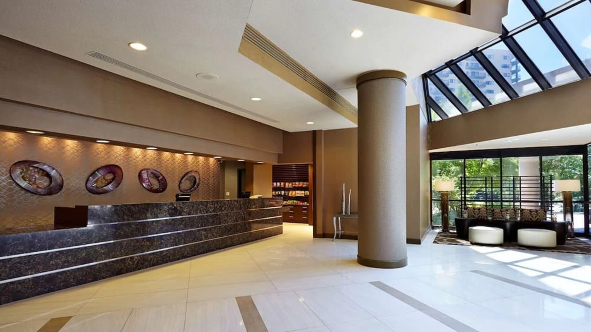 Modern reception area featuring a spacious front desk, contemporary décor, seating, and abundant natural light at Embassy Suites by Hilton Crystal City National Airport.