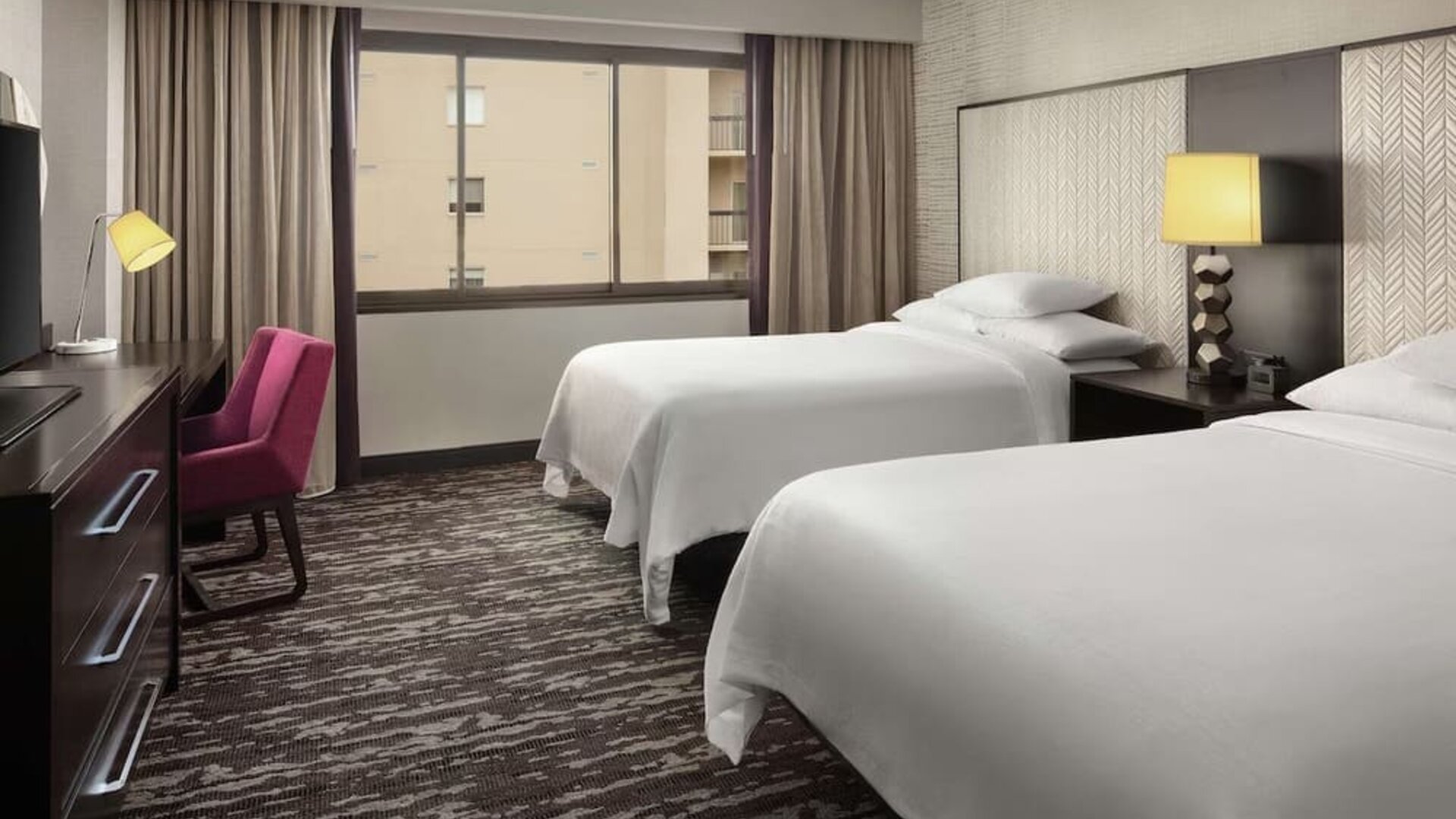 Comfortable guest room featuring two beds, dedicated workspace, television, large window, and contemporary décor at Embassy Suites by Hilton Crystal City National Airport.
