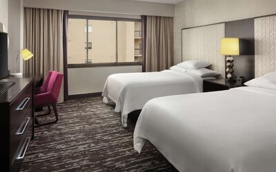 Comfortable guest room featuring two beds, dedicated workspace, television, large window, and contemporary décor at Embassy Suites by Hilton Crystal City National Airport.
