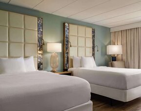 Comfortable guest room featuring two beds, modern headboards, bedside lighting, an armchair, and large window at Wyndham Garden Pittsburgh Airport.