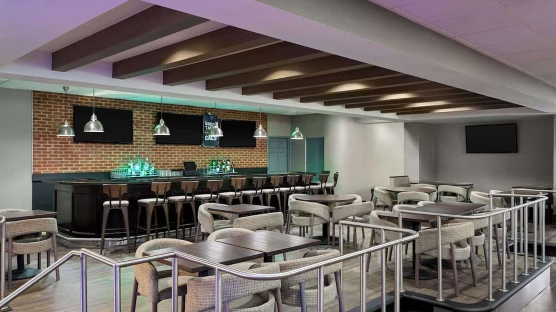 Spacious hotel bar and lounge featuring bar seating, dining tables, televisions, pendant lighting, and contemporary furnishings at Wyndham Garden Pittsburgh Airport.