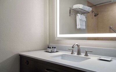 Modern guest bathroom vanity featuring a spacious countertop, illuminated mirror, toiletries, and contemporary fixtures at Wyndham Garden Pittsburgh Airport.