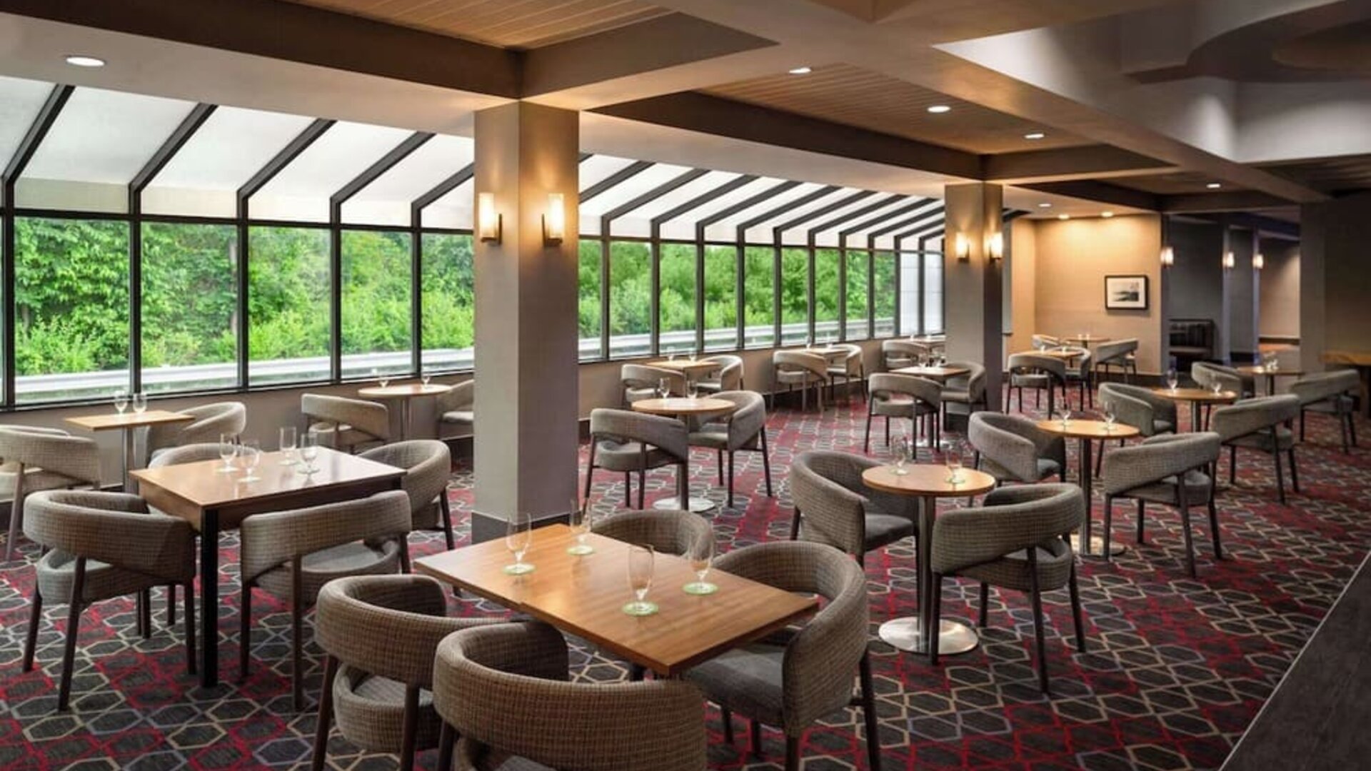 Spacious hotel dining area featuring multiple tables, comfortable seating, and expansive windows overlooking lush greenery at Wyndham Garden Pittsburgh Airport.