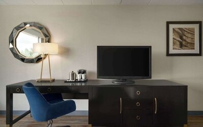 In-room workspace featuring a large desk, ergonomic chair, television, coffee station, mirror, and desk lamp at Wyndham Garden Pittsburgh Airport.