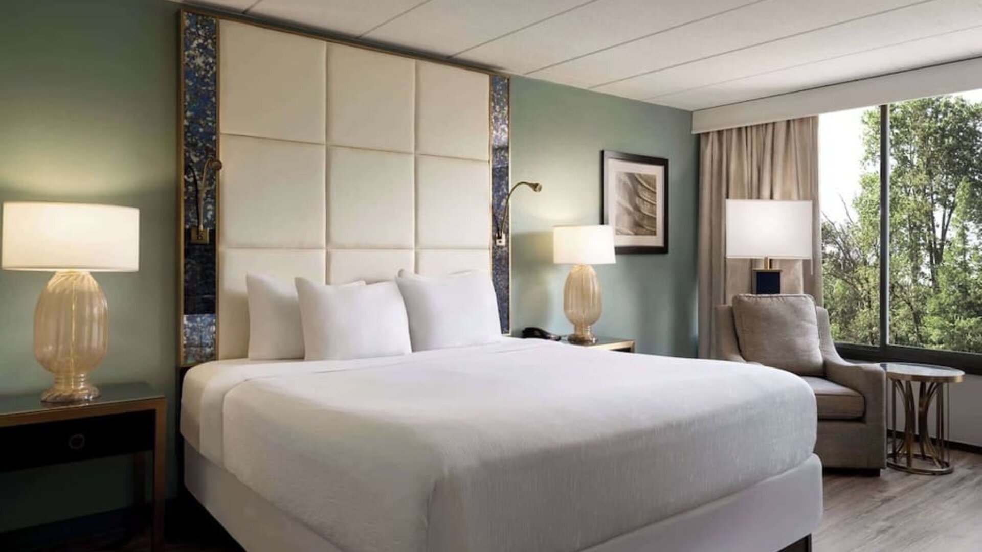 Comfortable king guest room featuring a plush bed, bedside lighting, armchair, and large window with natural views at Wyndham Garden Pittsburgh Airport.