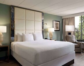 Comfortable king guest room featuring a plush bed, bedside lighting, armchair, and large window with natural views at Wyndham Garden Pittsburgh Airport.