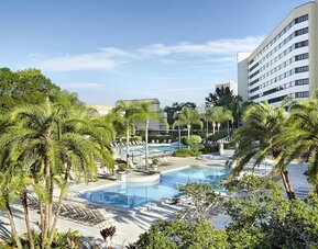 Outdoor pool, palm trees, and hotel exterior. 