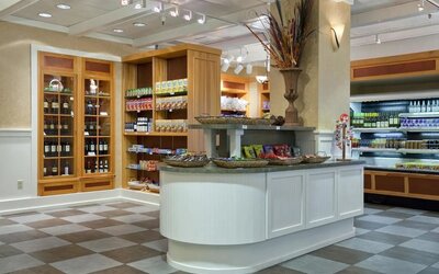 Hotel market with shelves of packaged snacks and beverages, wine display cabinets, refrigerated cases, and a central counter with decorative baskets.