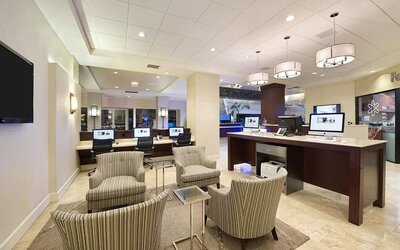 Spacious hotel business center with multiple desktop computers, a printer station, striped lounge chairs, small tables, and modern pendant lighting.