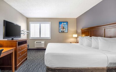 Bright king guest room featuring a large bed, television, workspace, window, and air-conditioning unit. Best Western McCarran Inn.