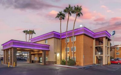 Exterior view featuring the hotel building, covered entrance, palm trees, parking area, and colourful evening sky. Best Western McCarran Inn.