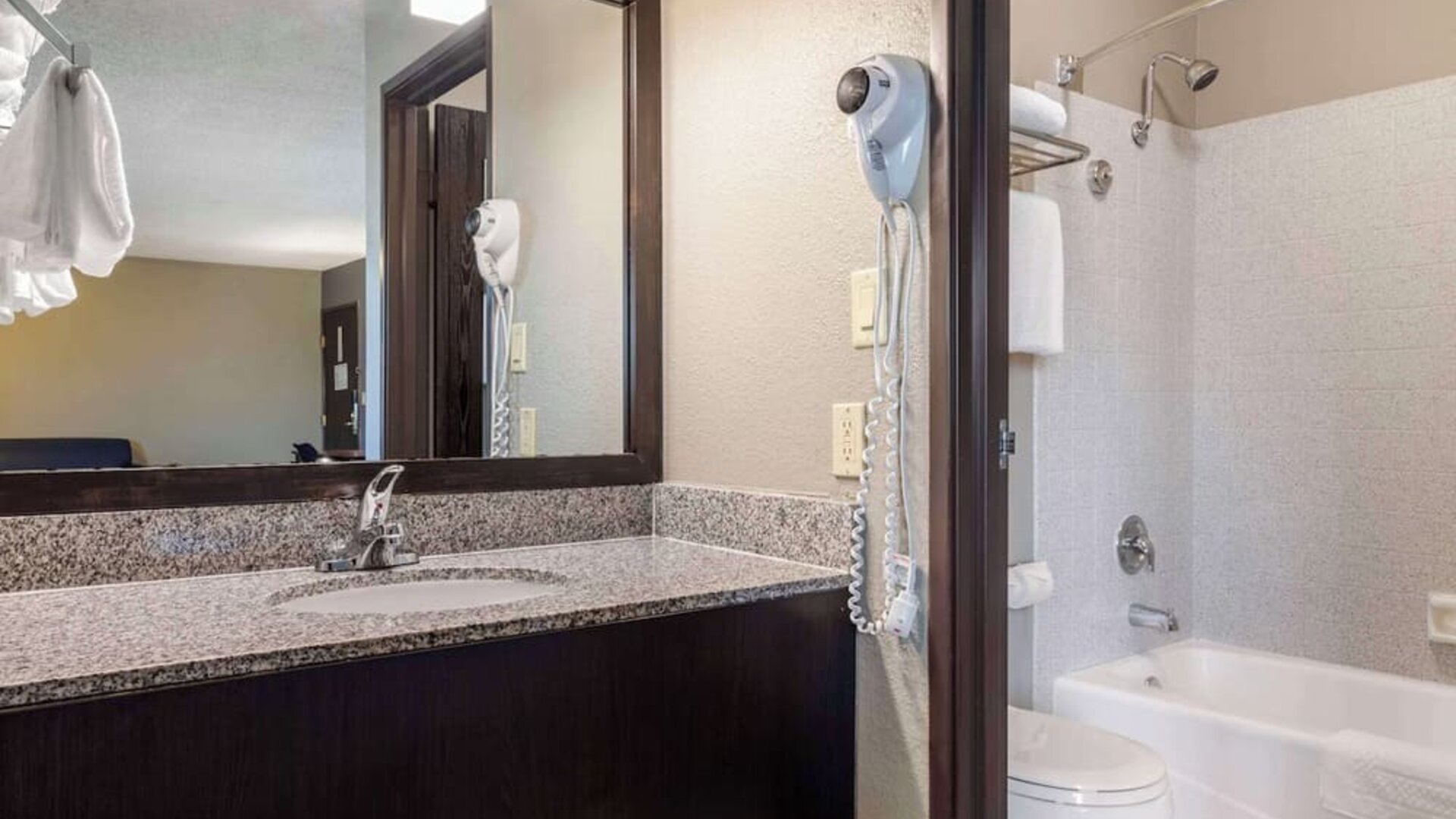 Guest bathroom featuring a granite vanity, large mirror, bathtub and shower combination, and wall-mounted hairdryer. Best Western McCarran Inn.