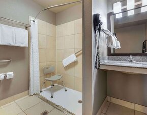 Accessible guest bathroom featuring a roll-in shower with shower chair, grab bars, vanity, mirror, and fresh towels. Best Western McCarran Inn.