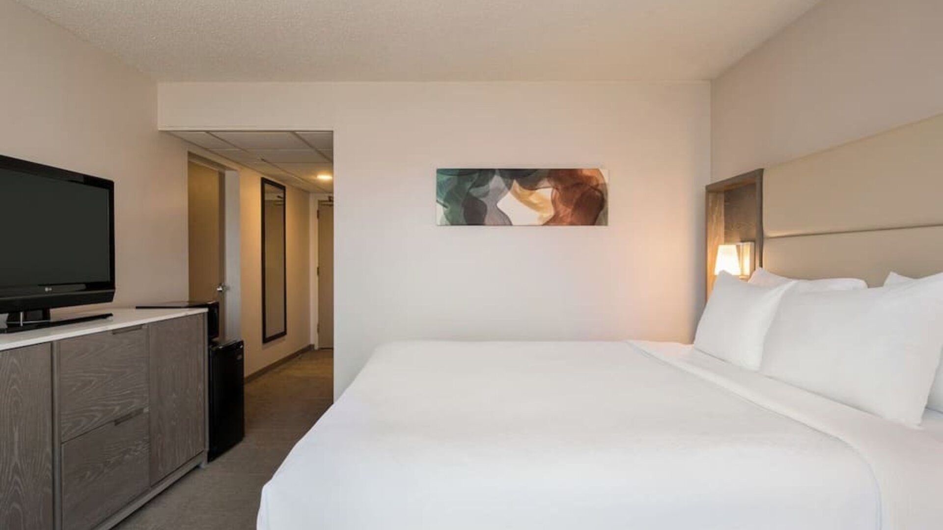 King guest room featuring a large bed, television, bedside lighting, storage cabinet, and contemporary artwork. Crowne Plaza Englewood.
