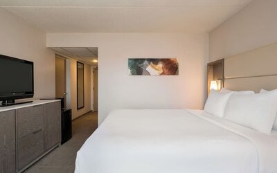 King guest room featuring a large bed, television, bedside lighting, storage cabinet, and contemporary artwork. Crowne Plaza Englewood.