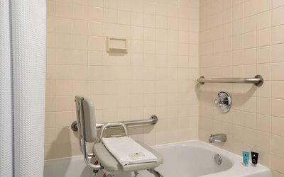Accessible bathroom featuring a bathtub with transfer bench, grab bars, shower curtain, and bath amenities. Crowne Plaza Englewood.