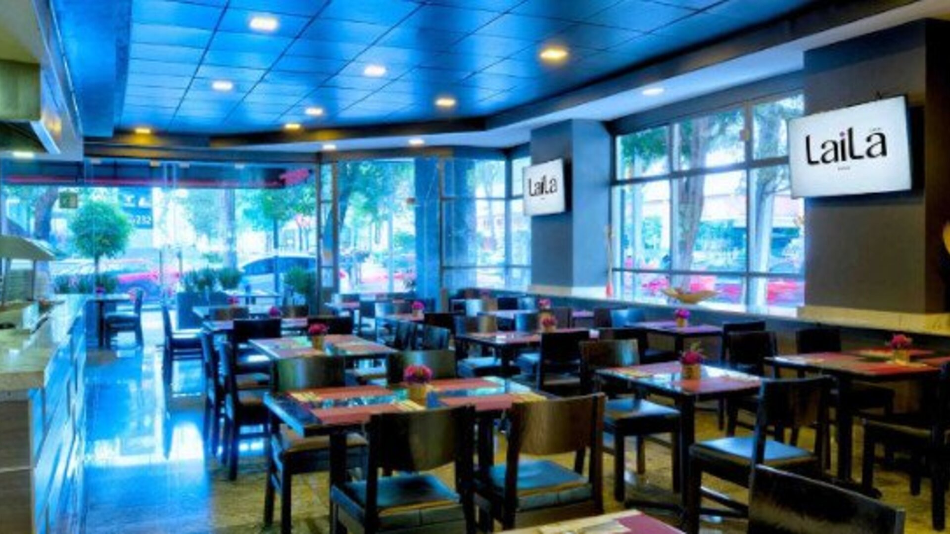 Stylish hotel lobby with black leather seating, mirrored walls and decorative overhead greenery. LaiLa Hotel CDMX.
