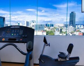 Fitness centre featuring cardio equipment and large windows overlooking the Mexico City skyline. LaiLa Hotel CDMX.