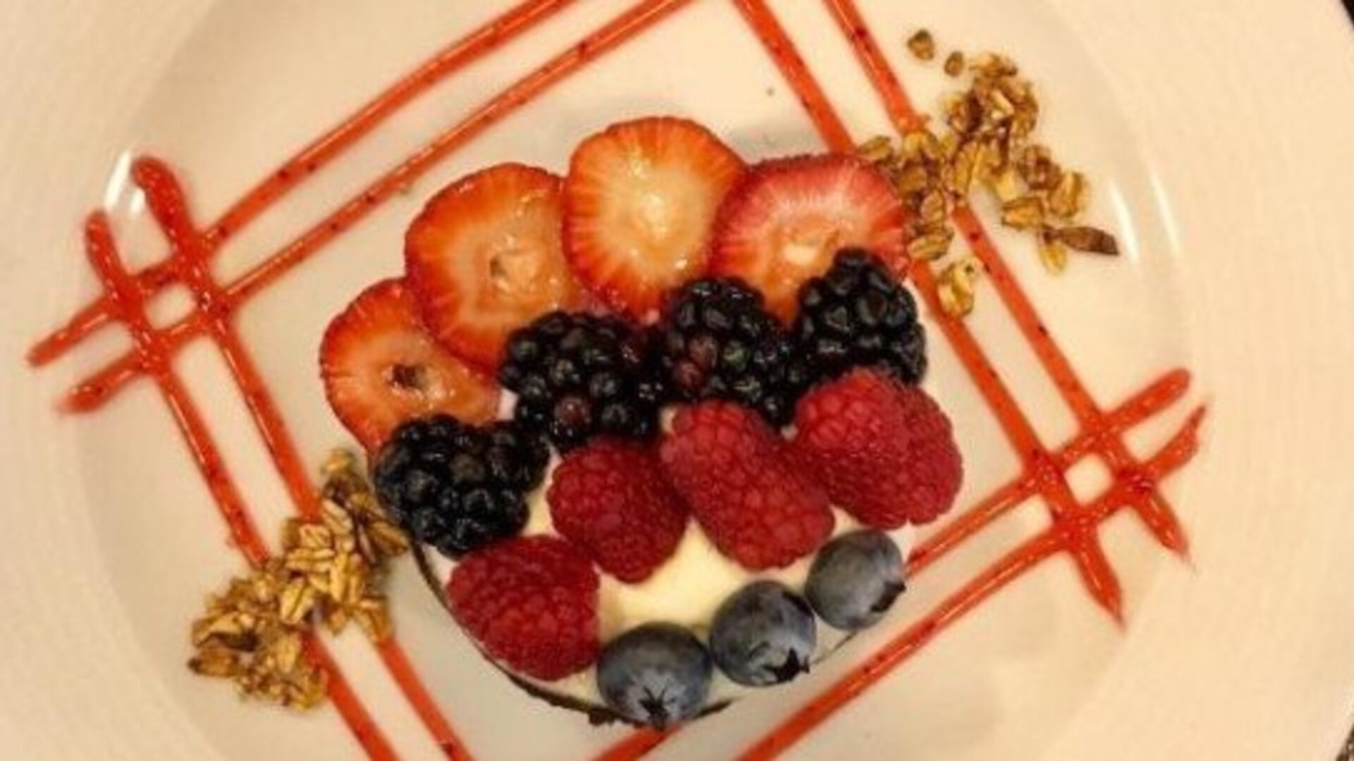 Elegant dessert topped with fresh strawberries, raspberries, blackberries and blueberries with decorative fruit sauce. LaiLa Hotel CDMX.