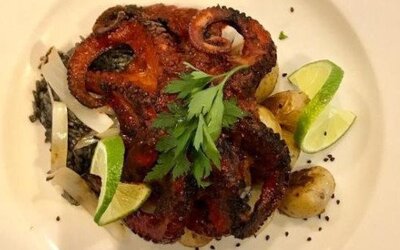 Grilled octopus dish served with lime wedges, roasted vegetables and fresh herbs. LaiLa Hotel CDMX.