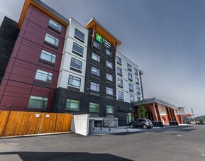 Exterior view of a modern Holiday Inn Express hotel with multi-story red, white, and dark stone façade, covered entrance, and adjacent parking area.