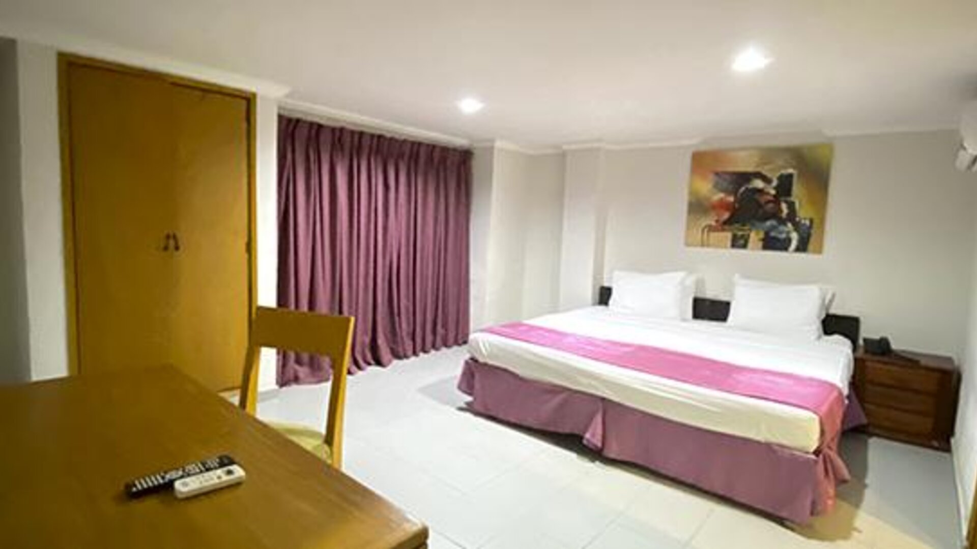 Spacious guest room with king bed, table, television and purple curtains at Hotel Puerta de Oro.