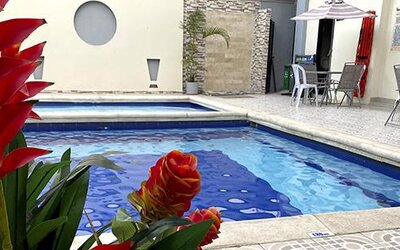 Outdoor swimming pool with tropical plants and patio seating at Hotel Puerta de Oro.
