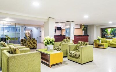 Hotel lobby with green armchairs, sofas, coffee tables and floral arrangements at Hotel Puerta de Oro.