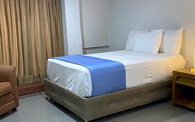 Guest room with double bed, armchair, bedside table and curtains at Hotel Puerta de Oro.
