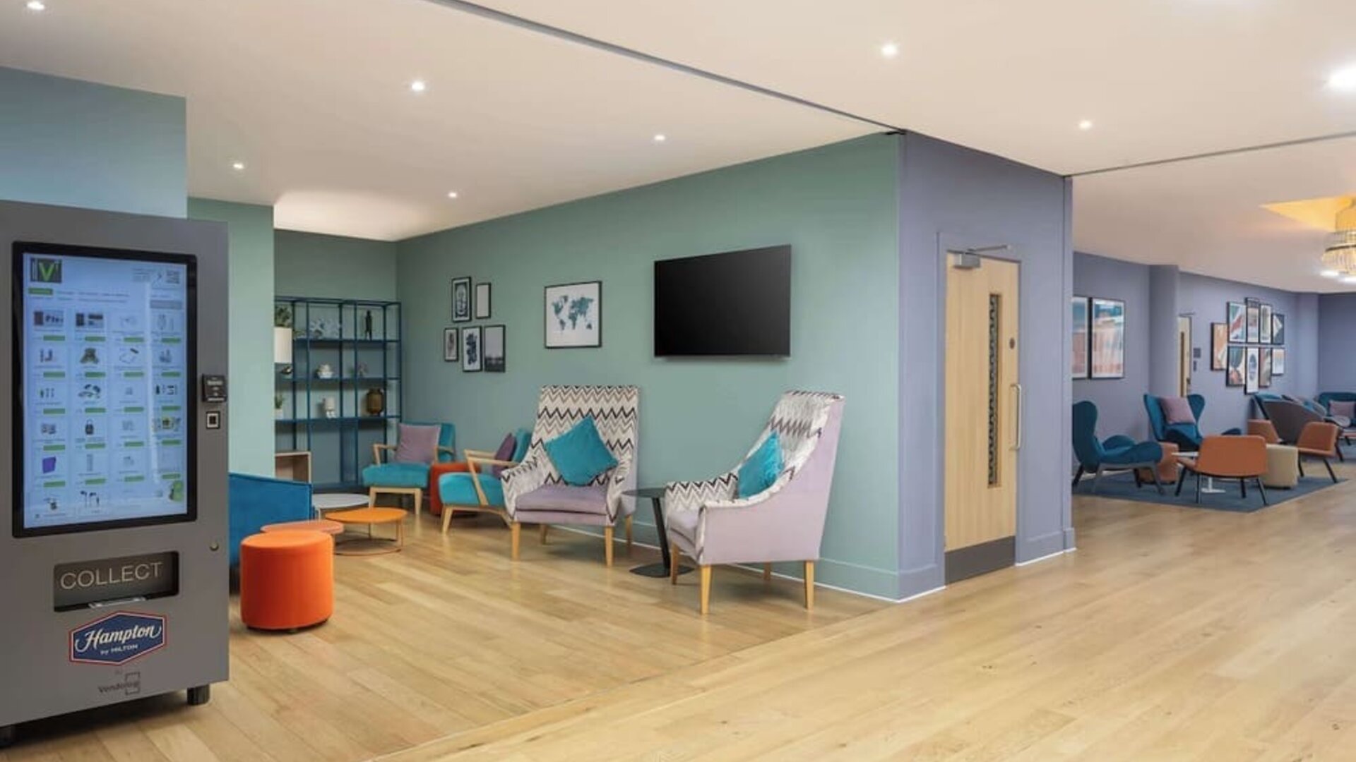 Colorful contemporary hotel lobby with teal and patterned lounge chairs, small tables, pale wood flooring, pastel green and blue walls and multiple seating areas.