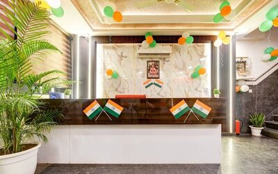 Hotel reception area decorated with Indian tricolor balloons and flags, featuring a dark wood and white front desk, marble-patterned feature wall, indoor plants and staircase to the side.