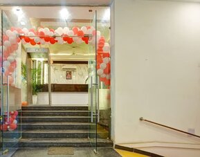 Glass entrance doors leading up several steps to the hotel reception area, decorated with an arch of red and white balloons, with a ramp and handrail visible to the right.
