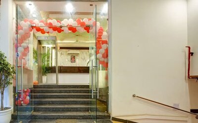 Glass entrance doors leading up several steps to the hotel reception area, decorated with an arch of red and white balloons, with a ramp and handrail visible to the right.