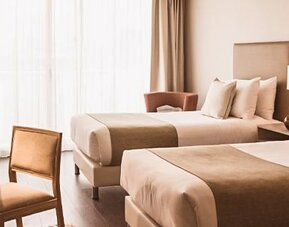 Guest room with two beds, a desk, armchair, bedside tables, and large windows with curtains at Dazzler by Wyndham Polo.