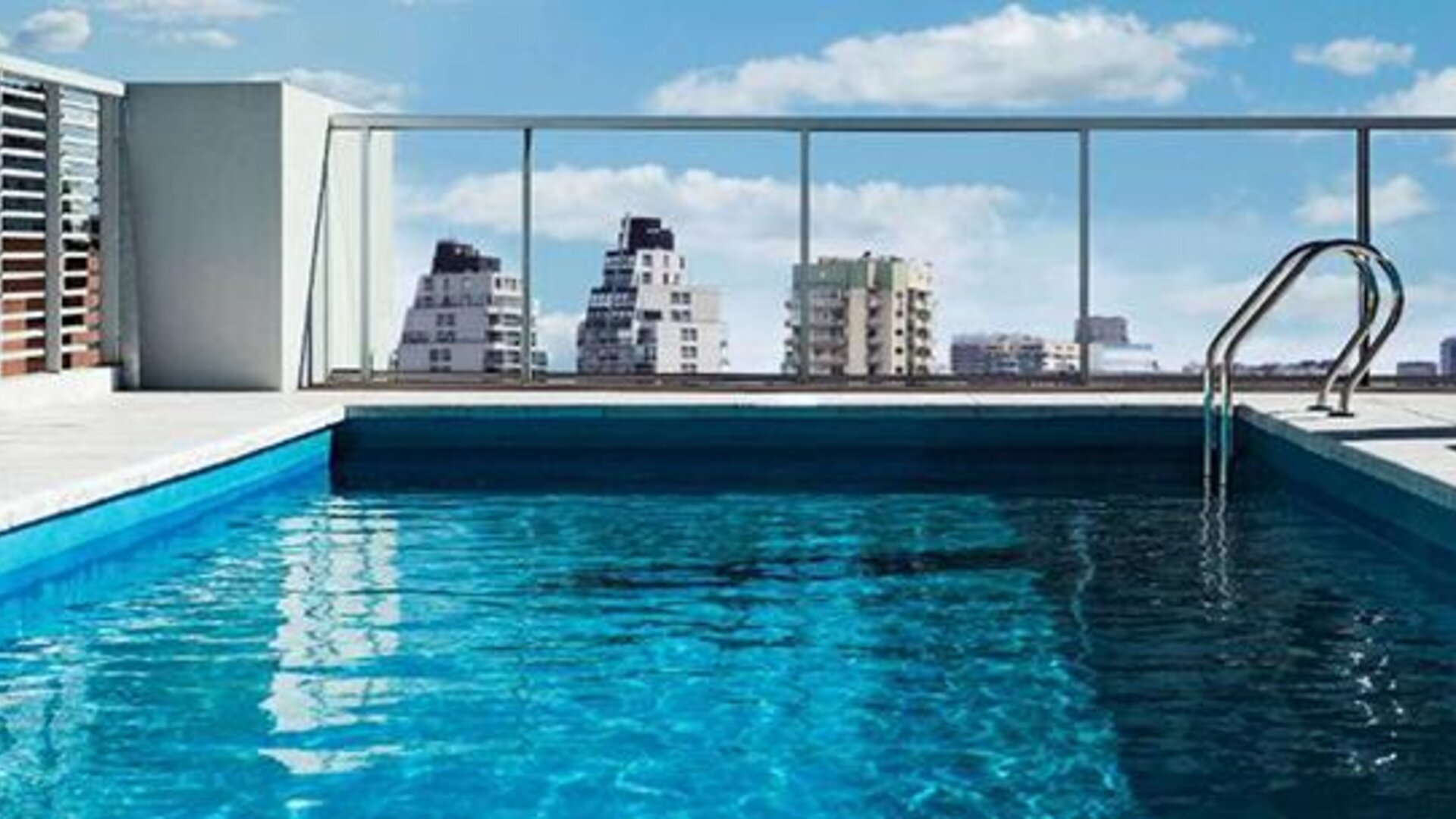 Rooftop swimming pool with a glass railing and views of surrounding city buildings at Dazzler by Wyndham Polo.