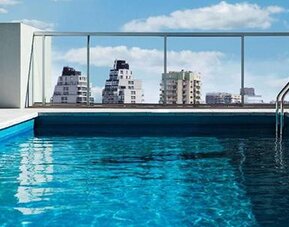 Rooftop swimming pool with a glass railing and views of surrounding city buildings at Dazzler by Wyndham Polo.