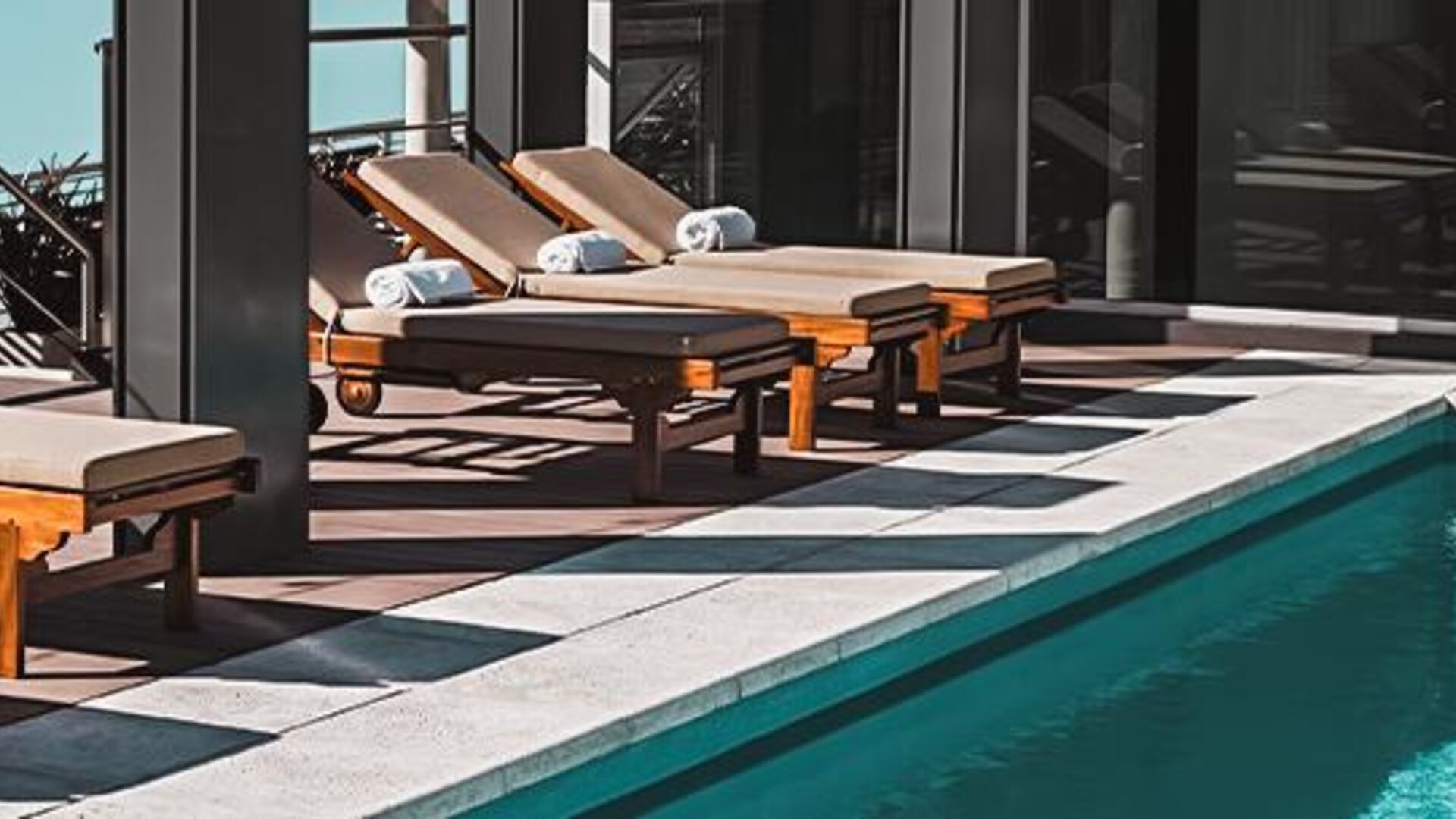 Outdoor pool deck with wooden loungers and folded towels beside a swimming pool at Dazzler by Wyndham Polo.