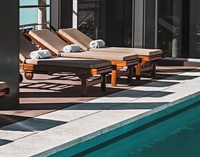 Outdoor pool deck with wooden loungers and folded towels beside a swimming pool at Dazzler by Wyndham Polo.