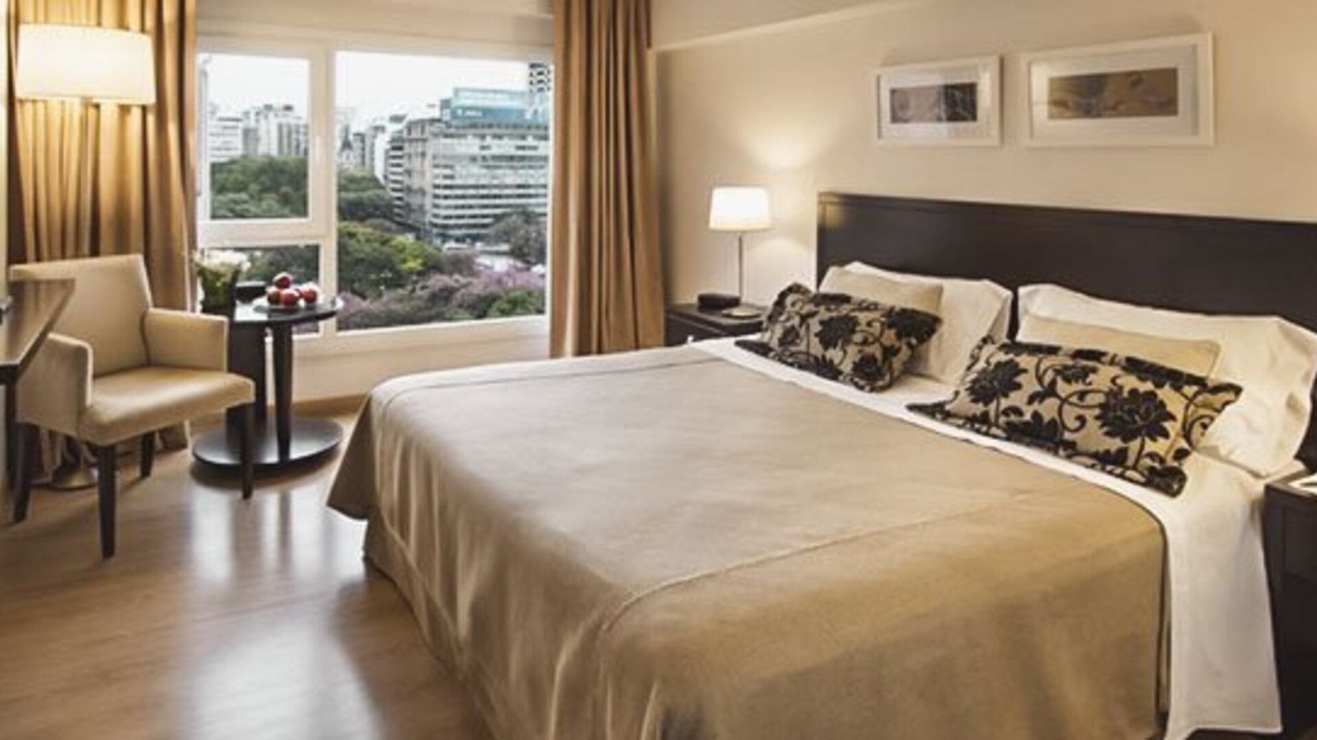 King-bed guest room with a large window overlooking city buildings, armchair, television, and bedside tables at El Conquistador Hotel.