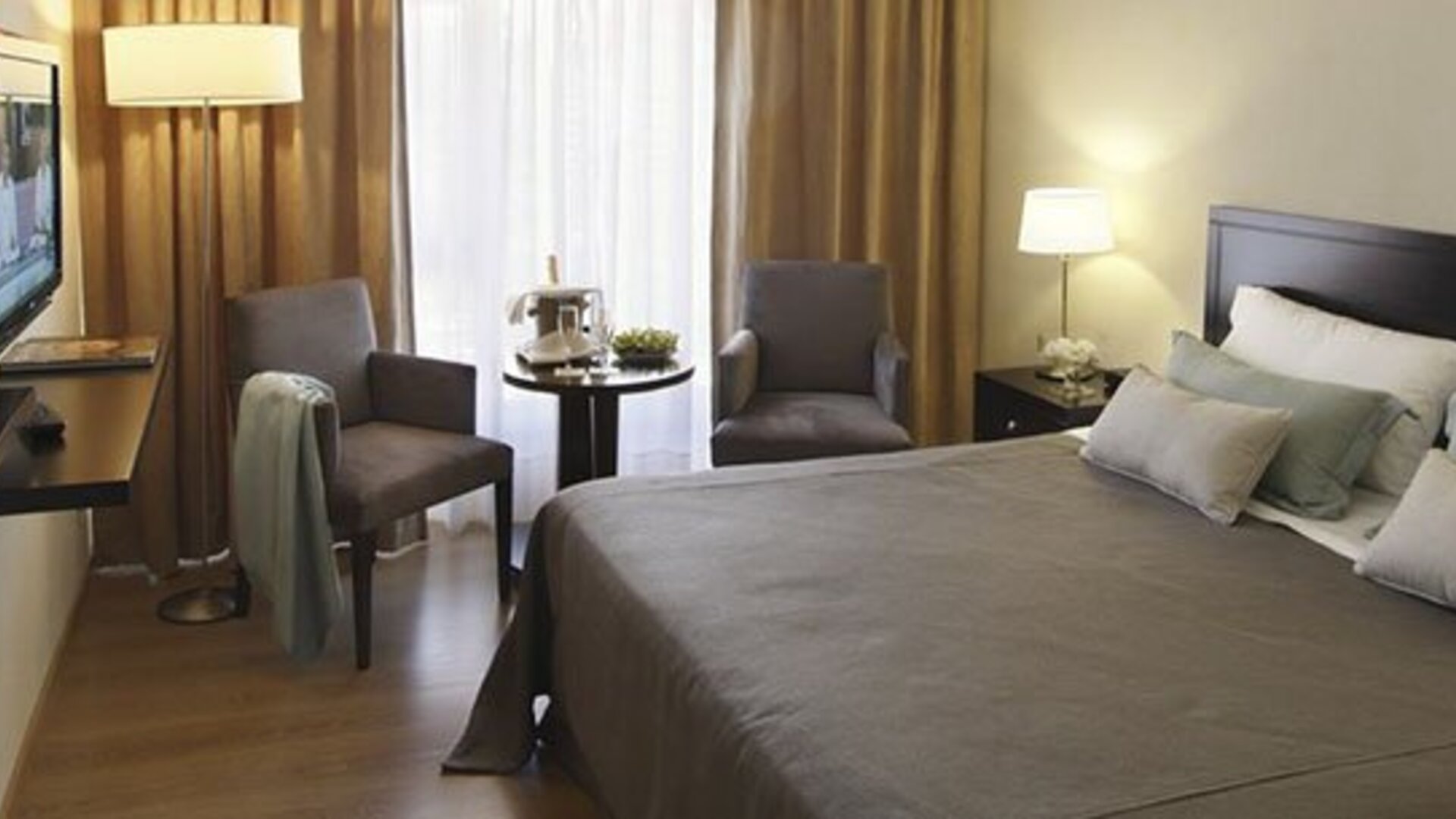 Guest room with a king bed, two armchairs, television, bedside table, and curtains at El Conquistador Hotel.