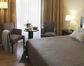 Guest room with a king bed, two armchairs, television, bedside table, and curtains at El Conquistador Hotel.