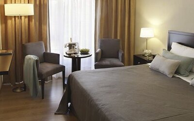 Guest room with a king bed, two armchairs, television, bedside table, and curtains at El Conquistador Hotel.